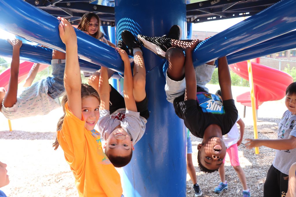 Kids hang from the jungle gym at a playground.