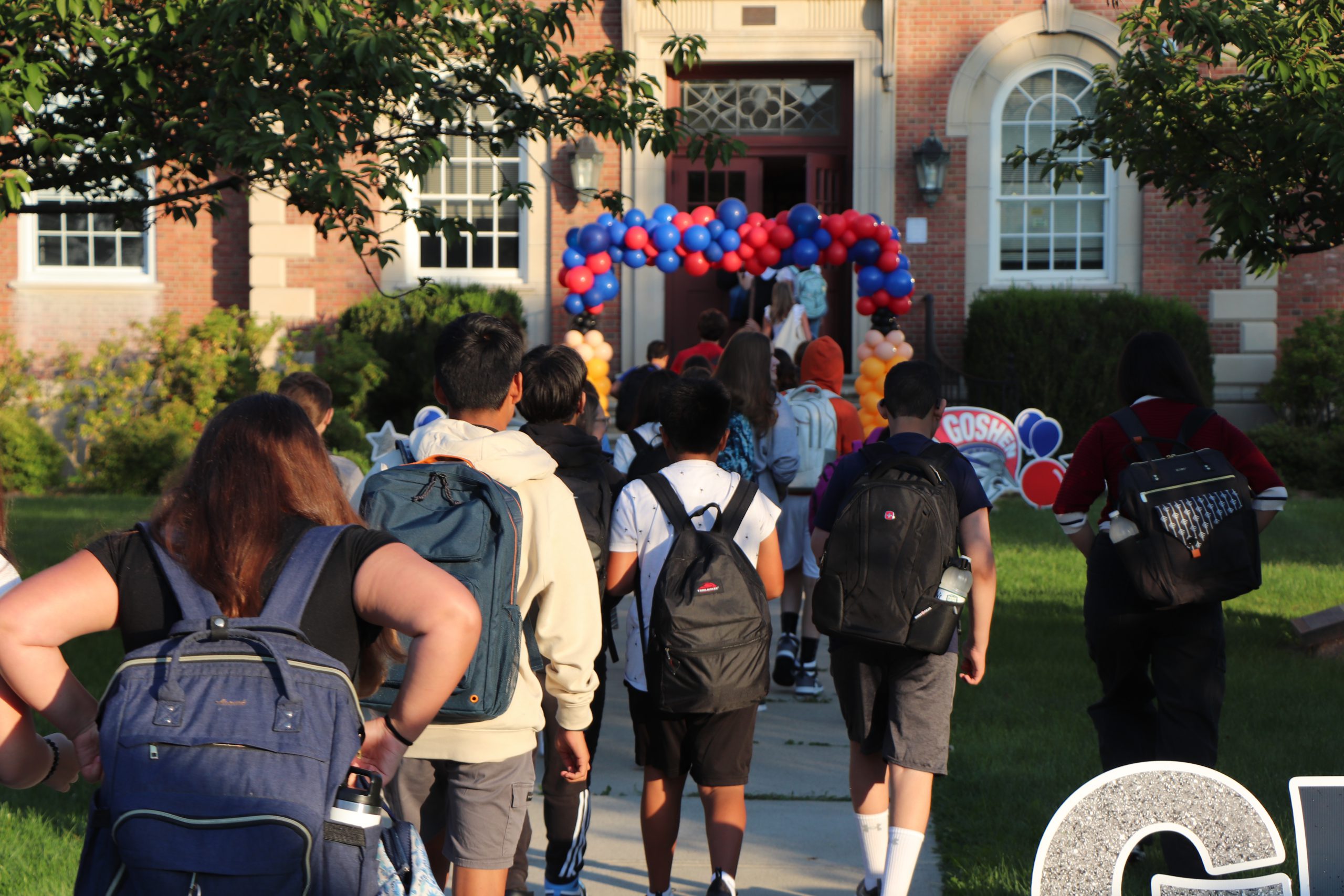 Preteens with backpacks walk toward a balloon arch in a school entry way.