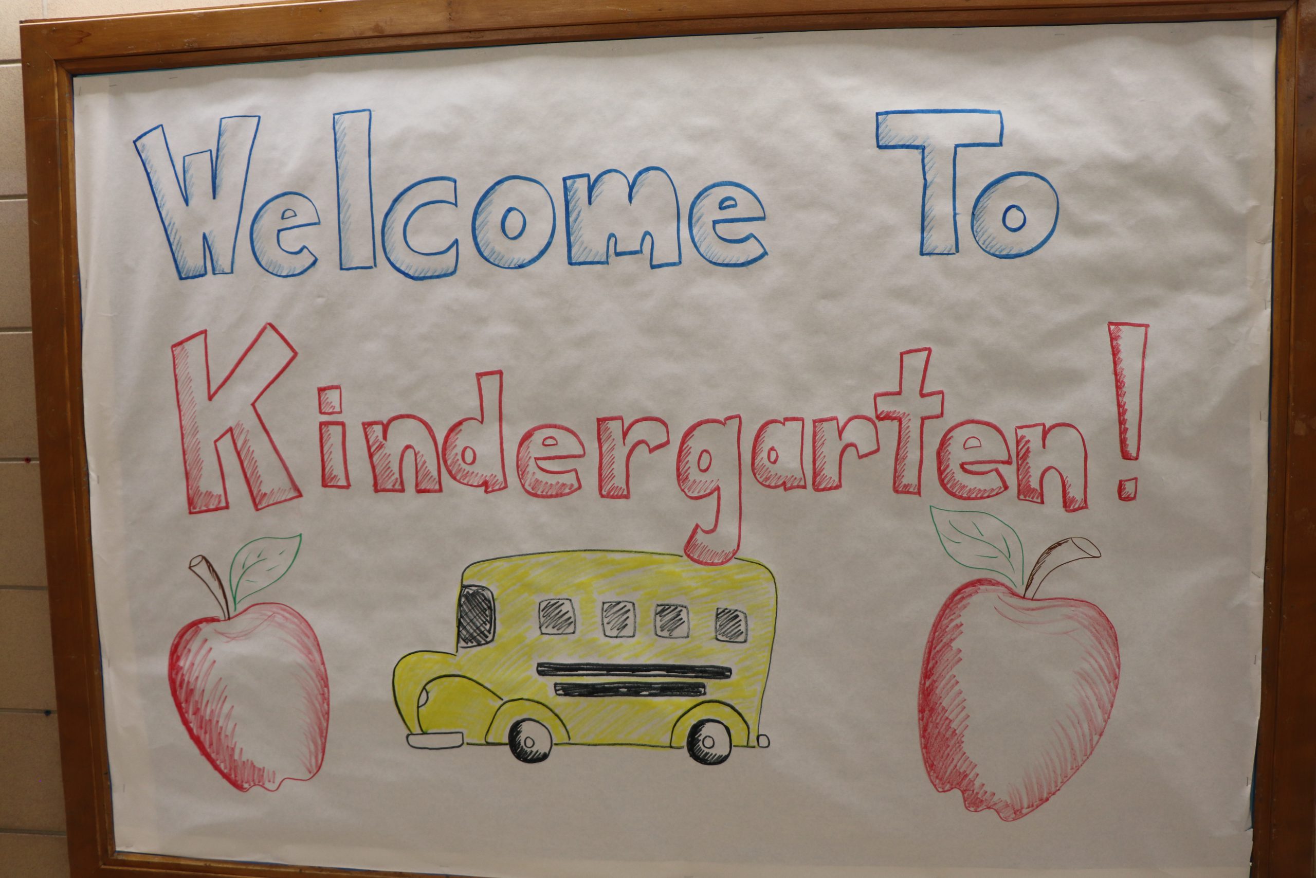 Sign that says "Welcome to Kindergarten" with an image of a school bus and two apples.