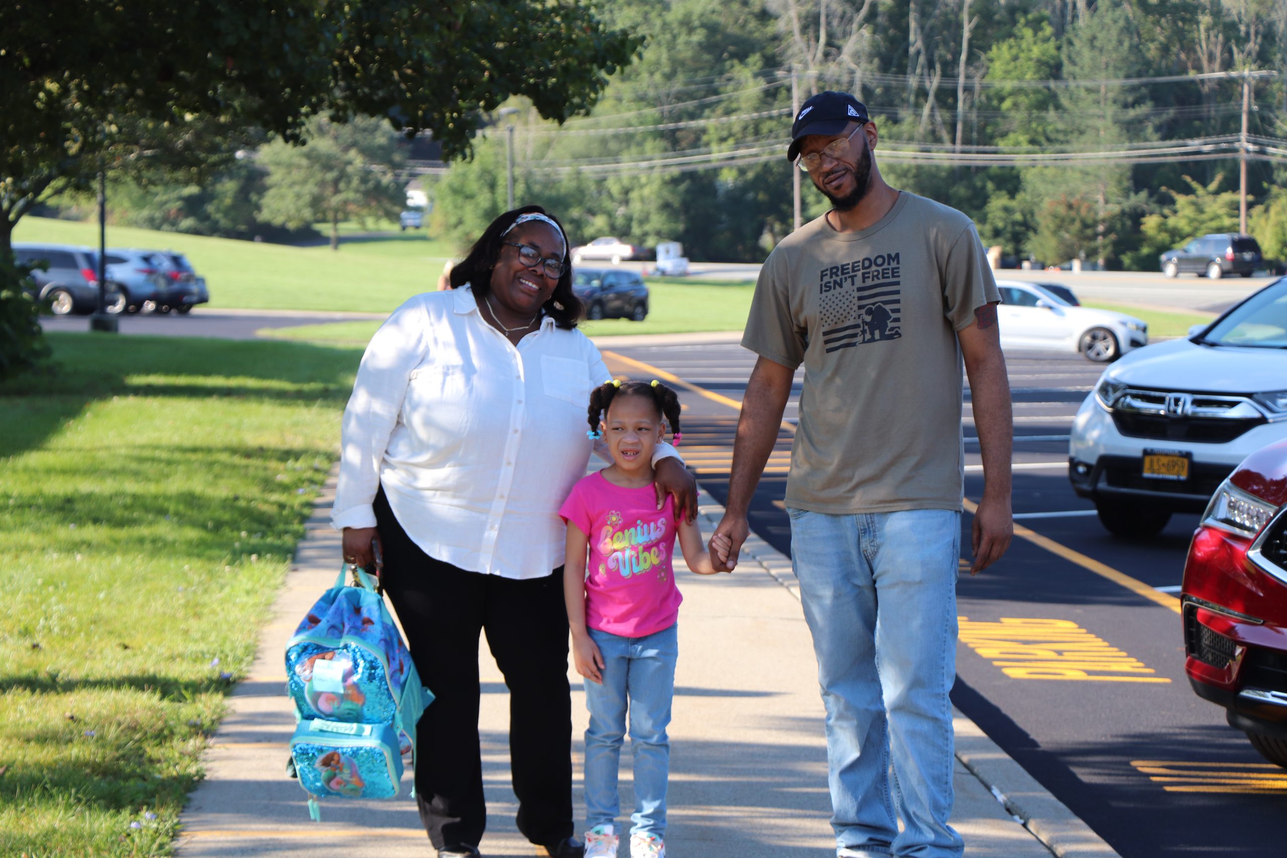 Two adults walk down a sidewalk with a child and their backpack.