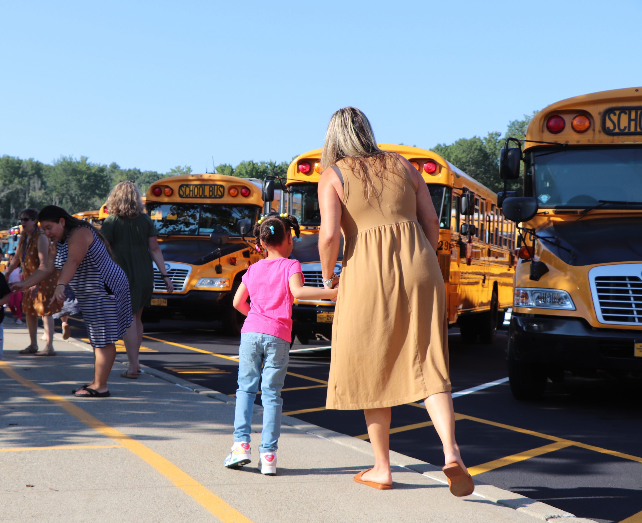 An adult and a child look out at school buses from the sidewalk.
