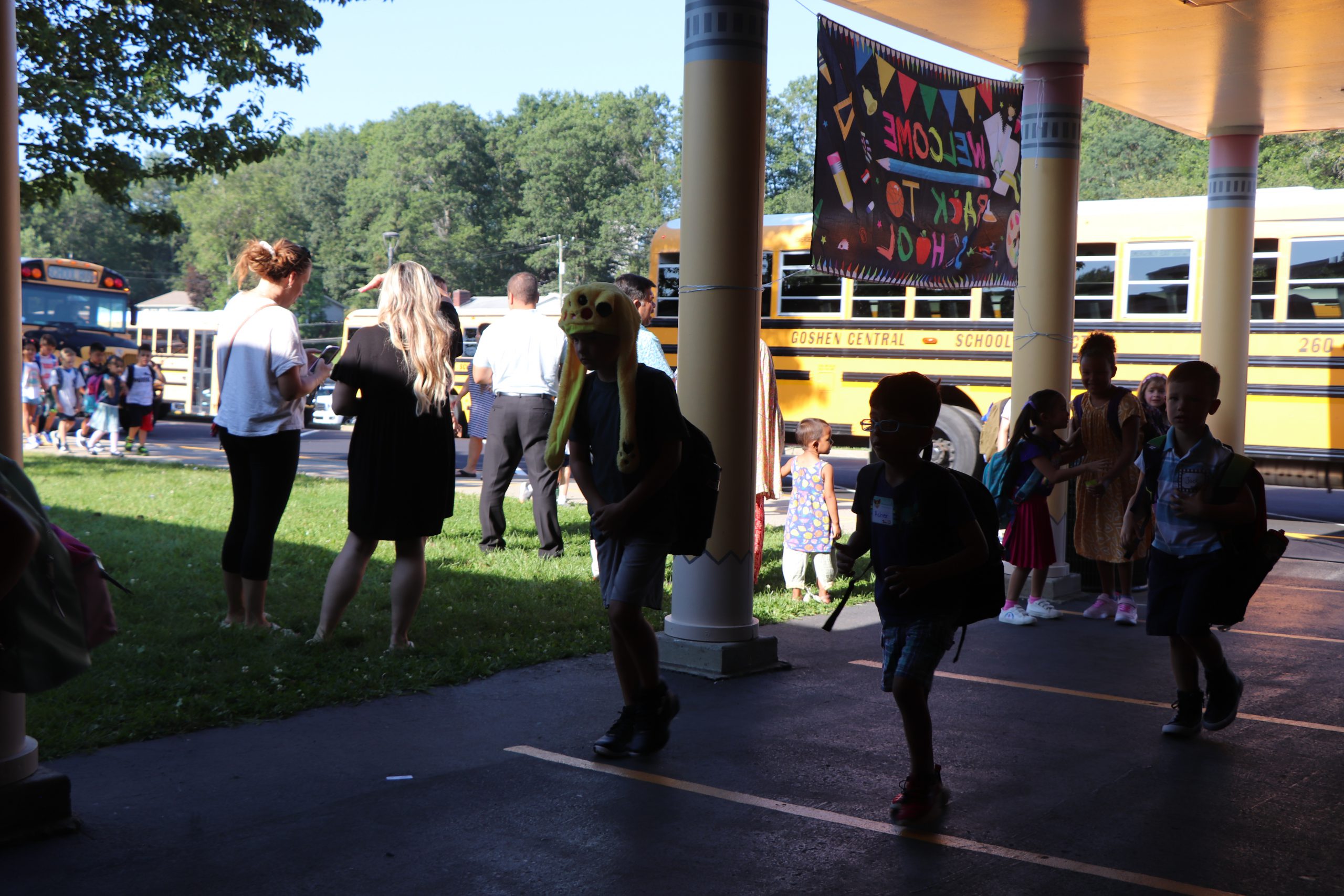 Children with backpacks walk past school buses together.