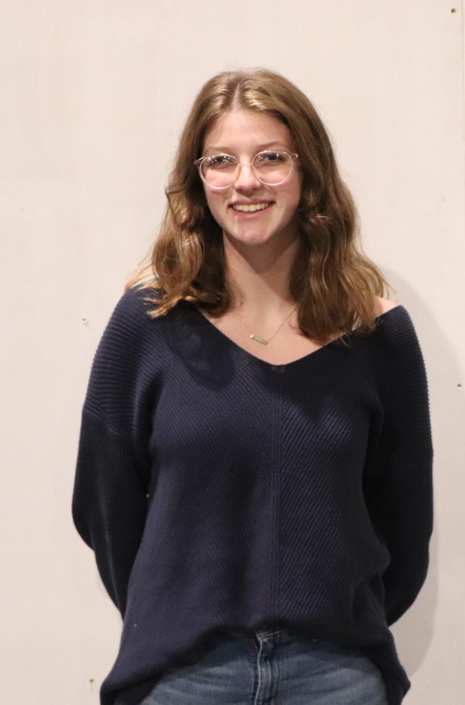 A teenager with glasses smiles in front of a white backdrop.