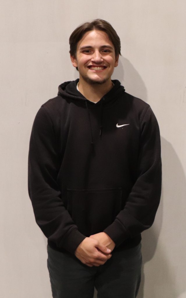 A teenager in a hoodie smiles in front of a white backdrop.