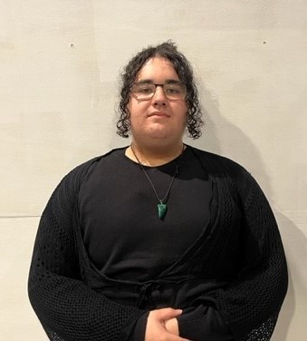 A teenager in a black shirt and knit wrap stands in front of a white backdrop.
