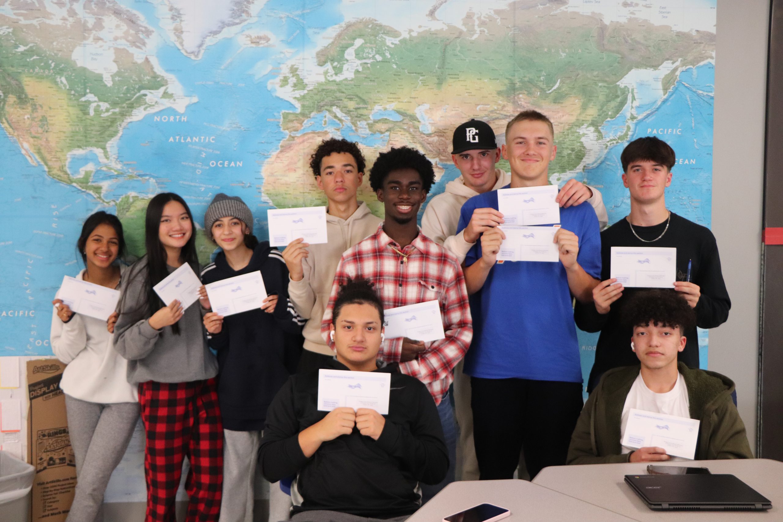 High school students stand together in front of a world map with their voter registration forms, smiling. 