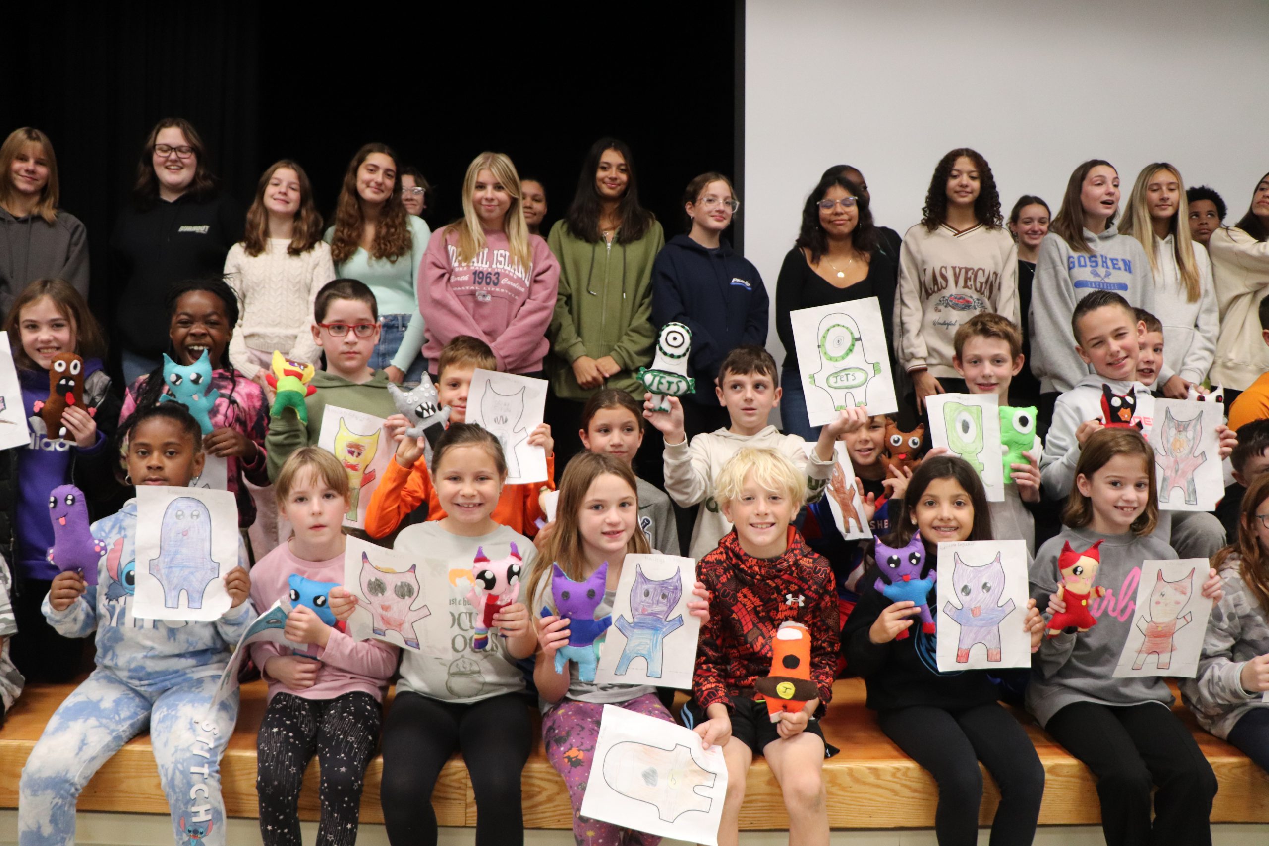 Elementary school and high school students stand together on a stage with handmade monsters, drawn by Goshen Intermediate School and handmade by Goshen High School.