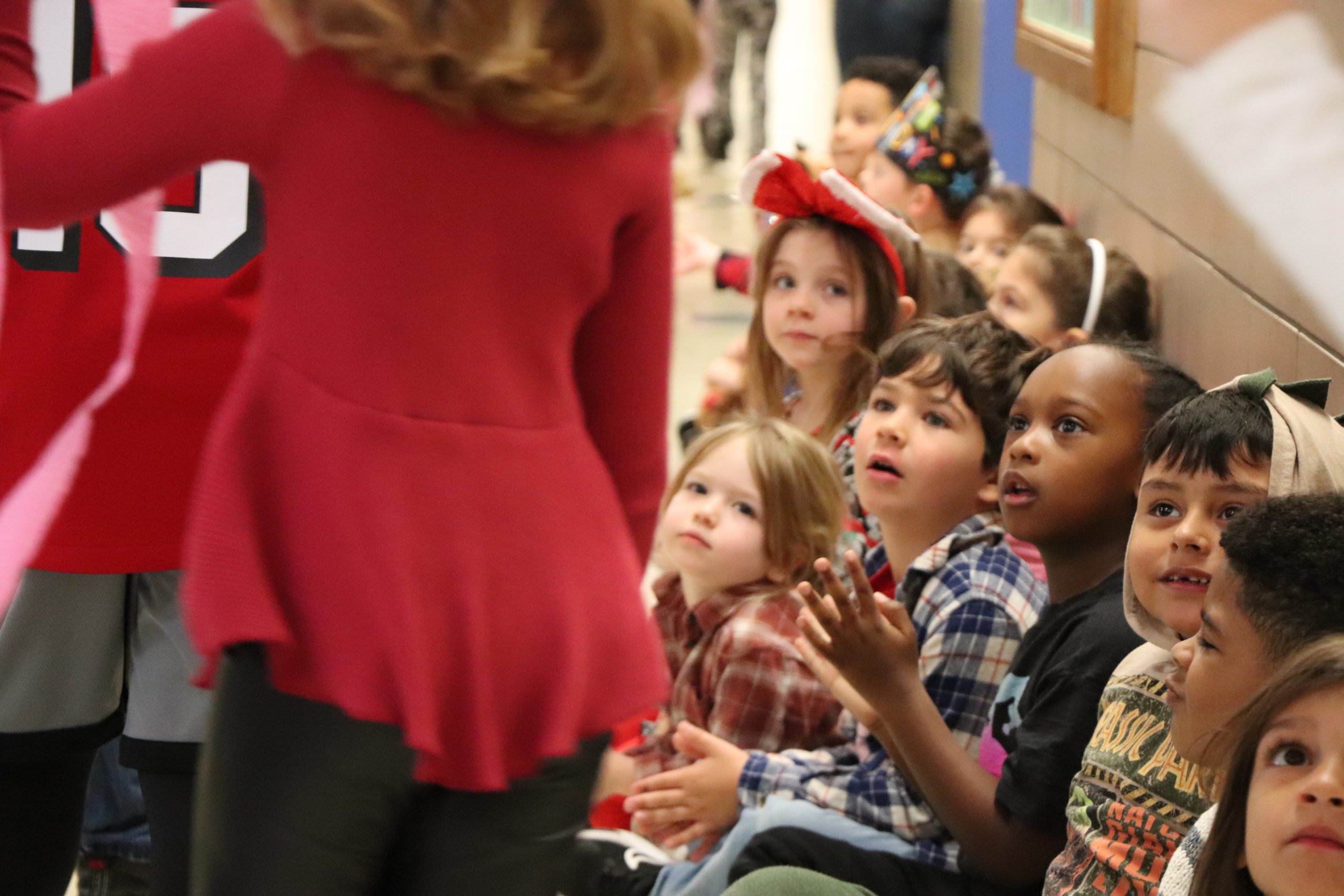 Elementary school students sit on the floor in a hallway mesmerized by the Thanksgiving parade at Scotchtown Avenue Elementary School.