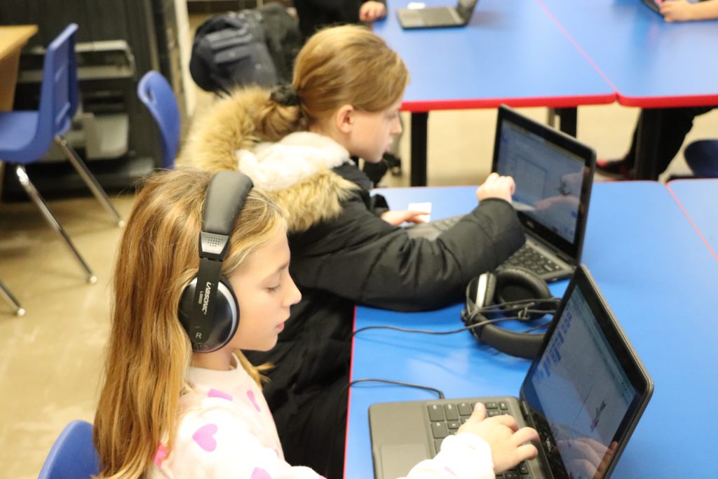 Two elementary school students wear headphones and work on Chromebooks during the last session of the Coding Club at Goshen Intermediate School.