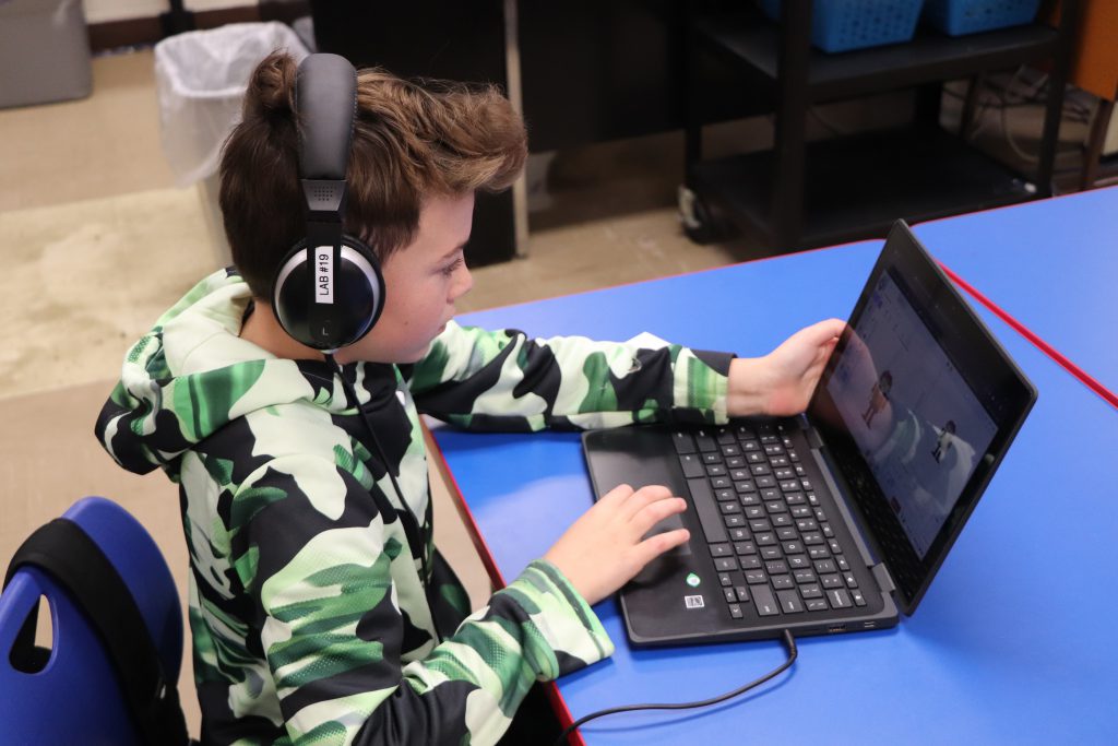 An elementary school student wears headphones and works on a Chromebook during the last session of the Coding Club at Goshen Intermediate School.