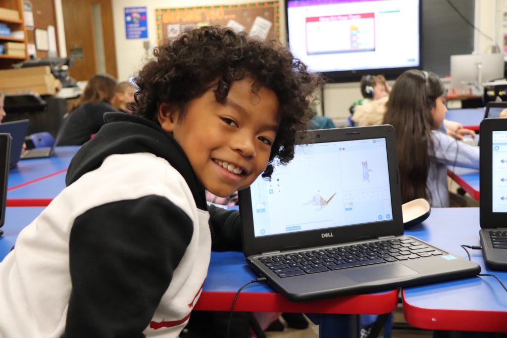 An elementary school student smiles next to his Chromebook screen depicting a dancing cat during the last session of the Coding Club at Goshen Intermediate School.