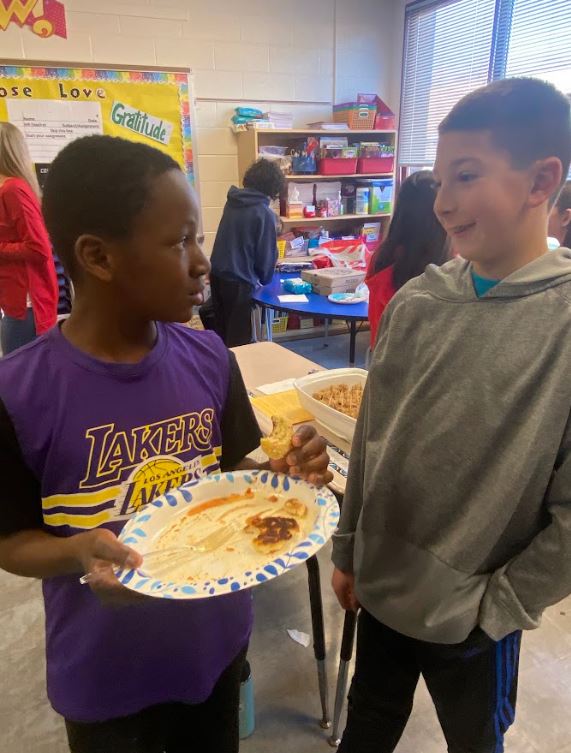 Two elementary school students mingle with food in a classroom during the GIS 5th Grade Culture Fest.
