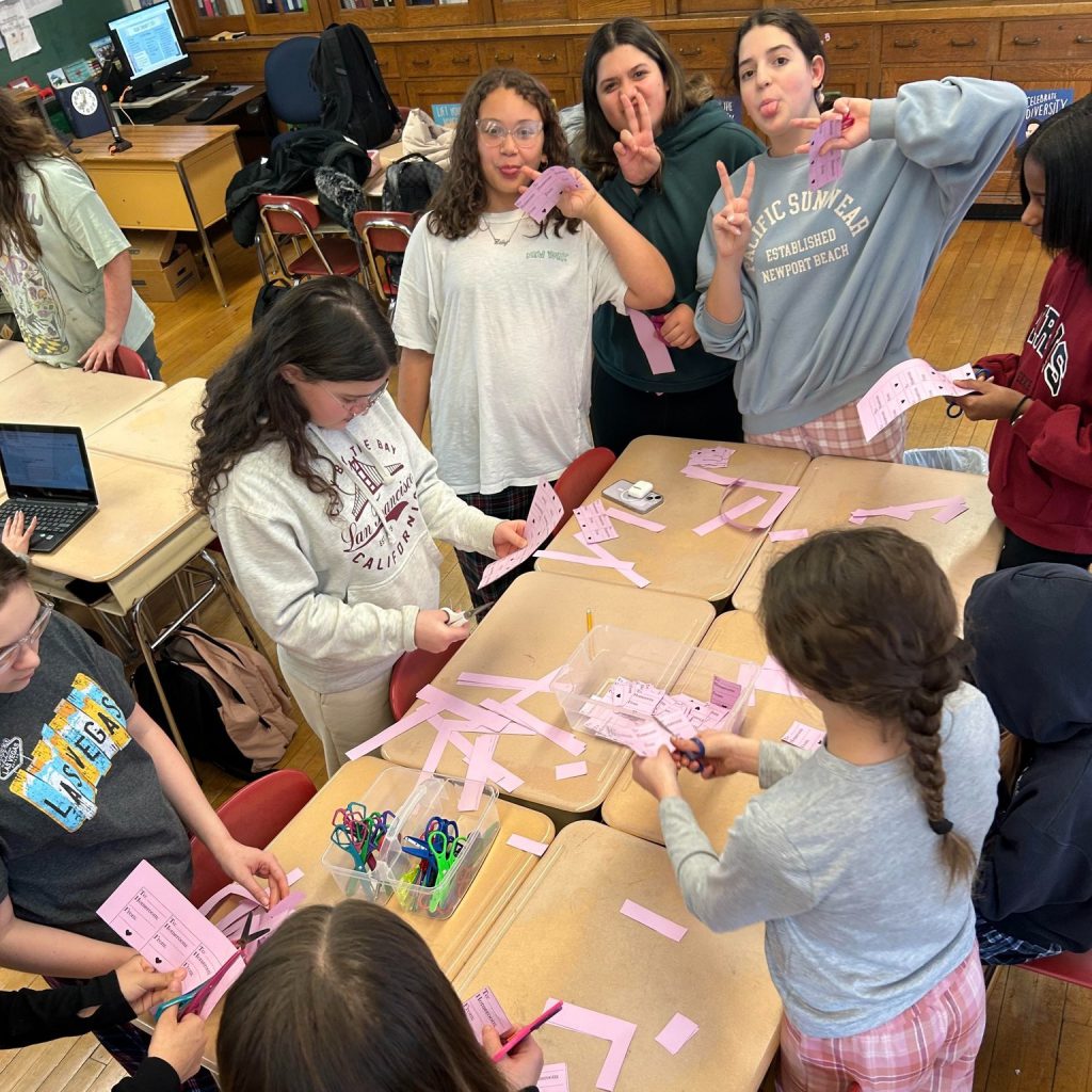 Middle school students cut Valentine's Day grams out of pink sheets of paper.
