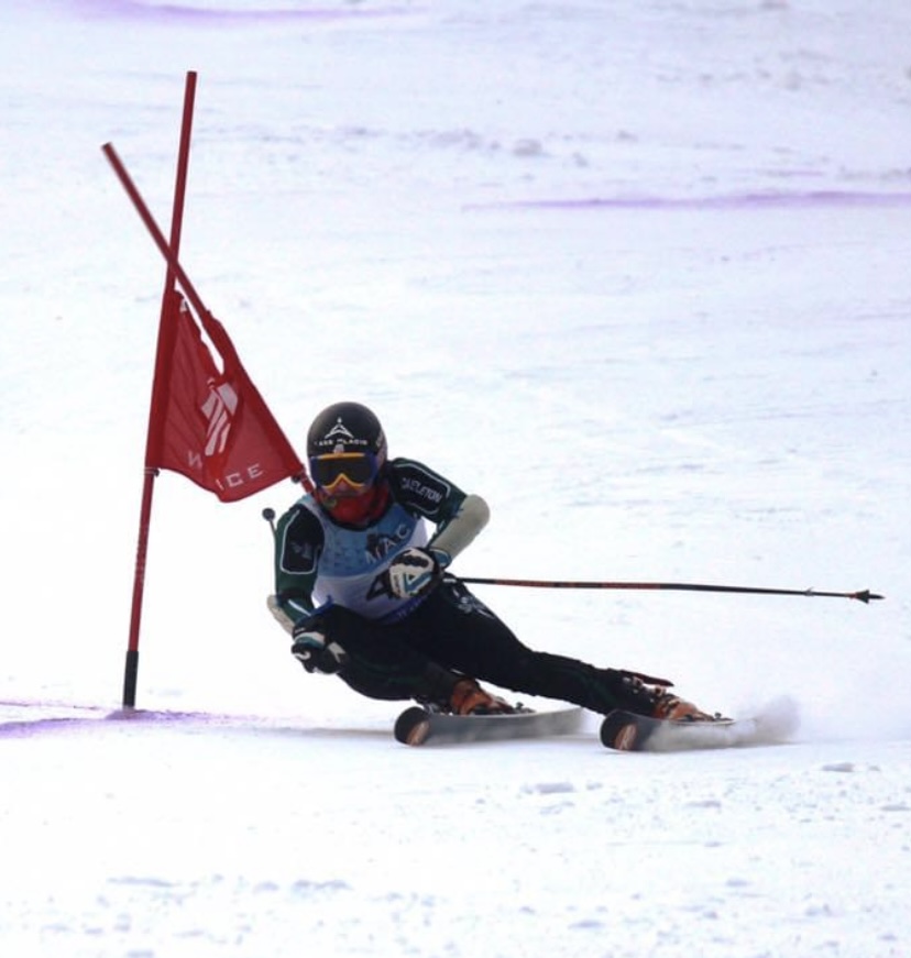 A man in ski gear races down a snowy slope next to a red flag.