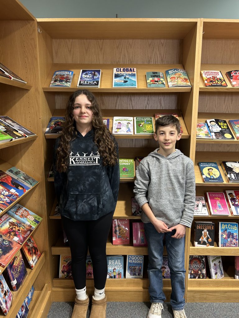Eighth grader Cora Massaro and seventh grader Luke Hand smile for a photo in front of a bookshelf.