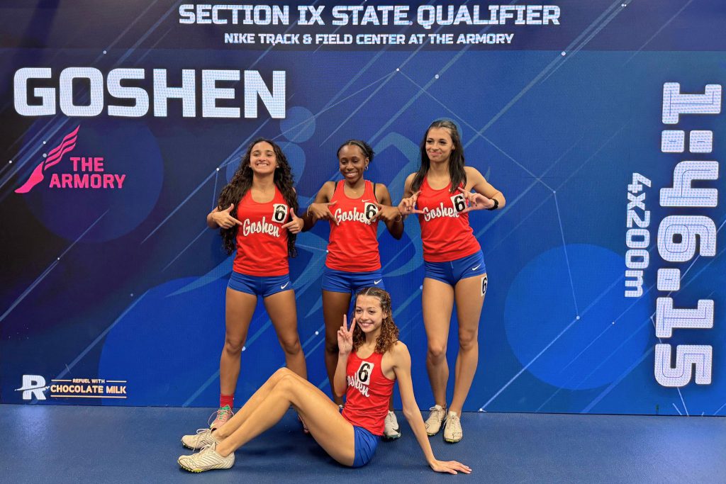 The girls 4x200-meter relay team celebrates at the section 9 qualifier event. There is a blue video board behind them displaying their time of 1:46.15 and the word Goshen.