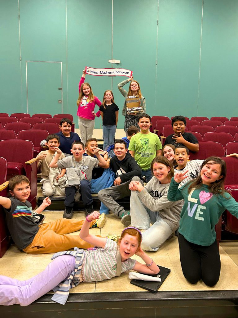 Mrs. Meocci's class poses with the champions in the background holding up their sign.