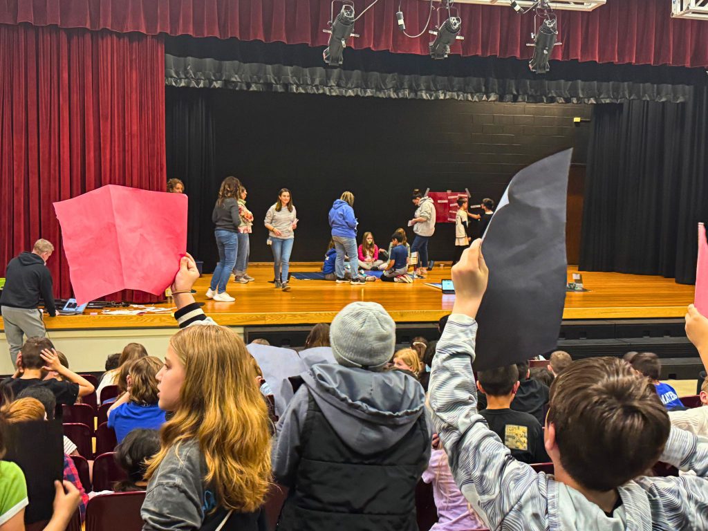 A view from behind the students in the crowd that are cheering on their classmates on stage.