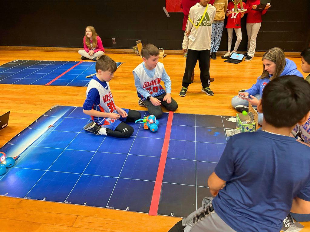Two students in Goshen jerseys are sitting near Dash during the competition.