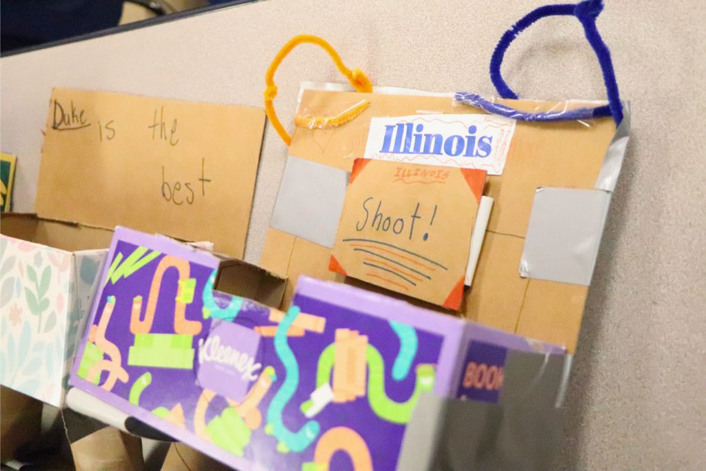 Two student made baskets are next to each other. One reads Duke is the best and the other has the Illinois team name printed out with the word "Shoot!" under it.