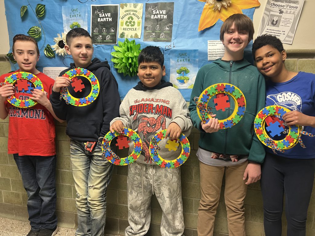 Five students stand together in front of a wall with handmade wreaths. They are smiling for the camera.