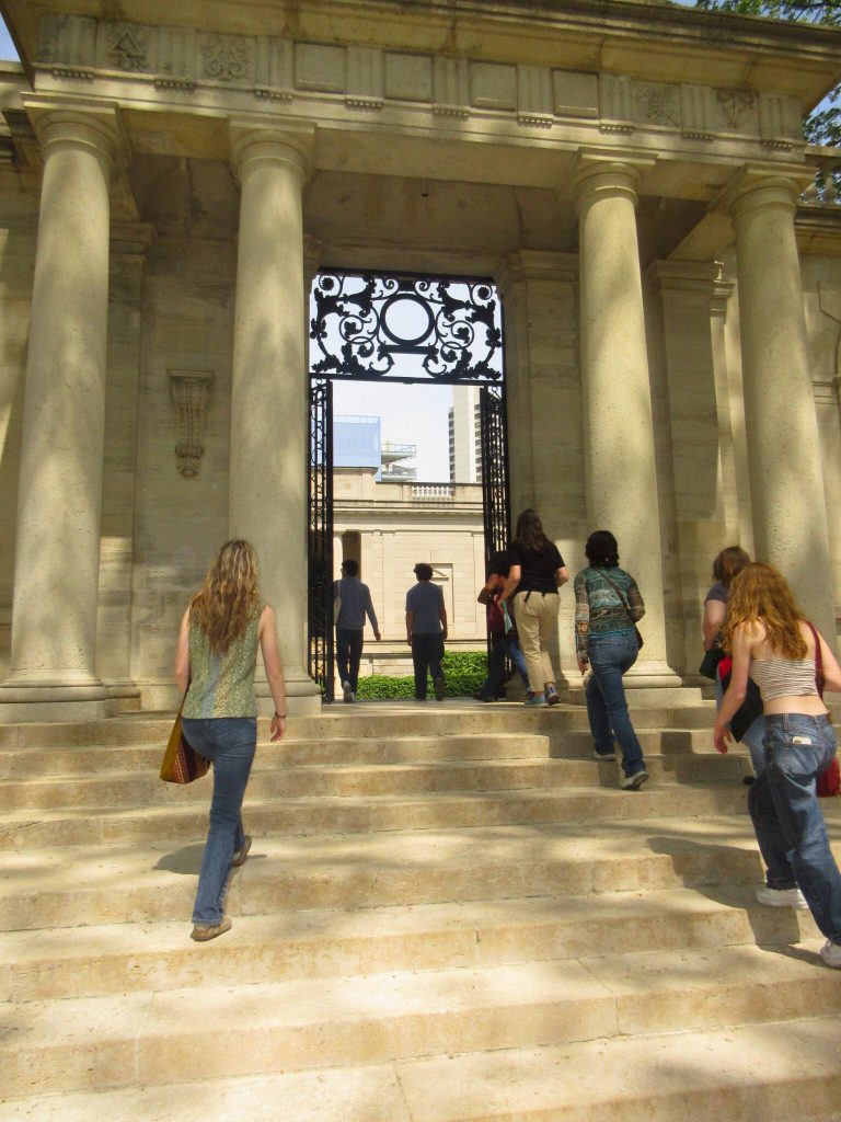 Students walking under a marble column opening heading toward and outside area.
