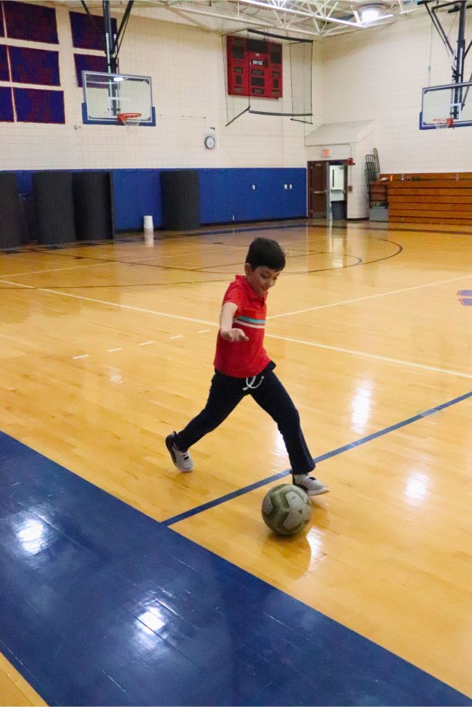 A student is kicking a soccer ball down the side of a court during practice for the Elementary Special Olympics.