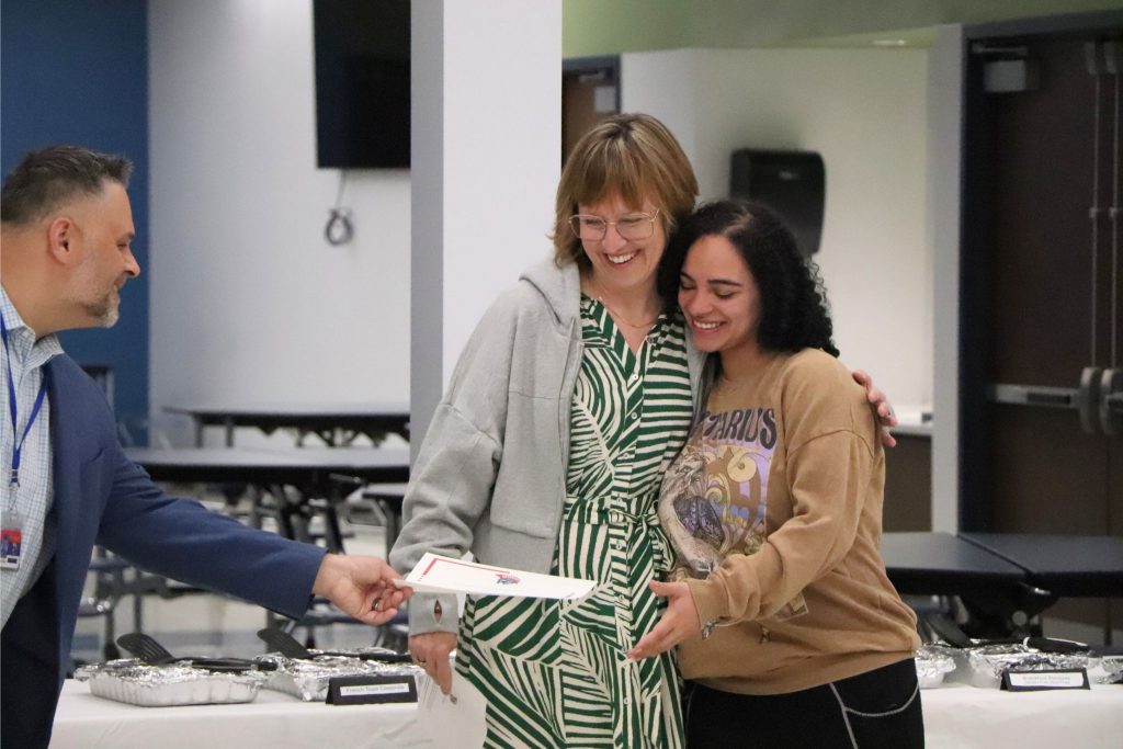 A teacher gives a hug to a student as the principal, Mr. Pantaleone, gives her a certificate.