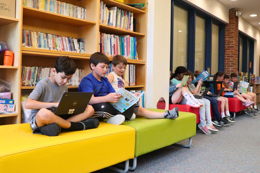 Students sit in next to each other along a wall on the Scotchtown Avenue Library's new furniture. The furniture is bright colors of yellow, green, blue and red.