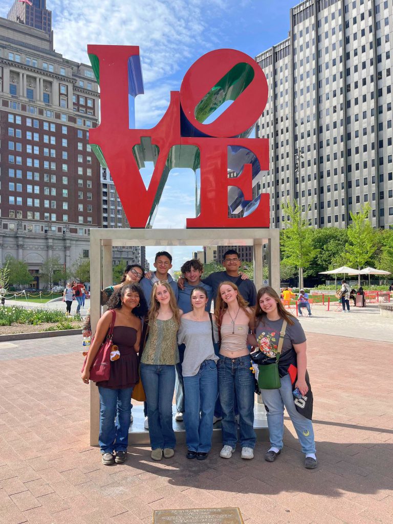 10 students pose for a photo under a sign that says love above them.