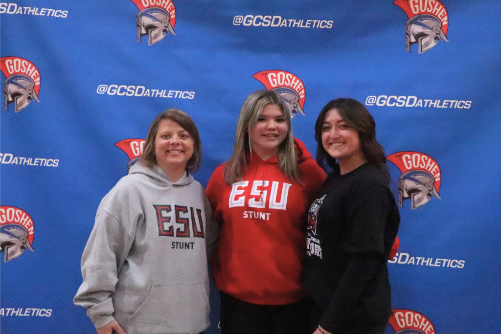 Hope Miller stands and smiles with her family with a Goshen background. They are wearing ESU sweaters.
