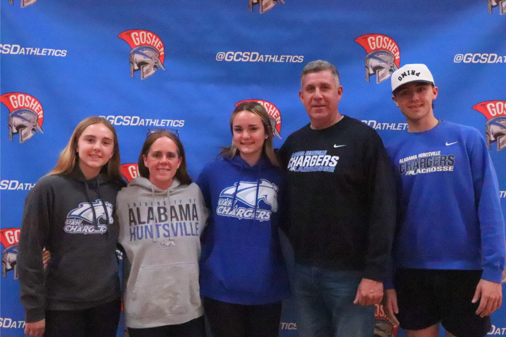 Meghan Doody smiles with her family for a picture. They are all wearing University of Alabama Huntsville shirts and sweaters.