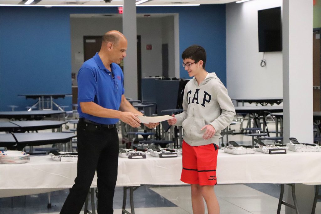 A student receives a certificate from his teacher in the cafeteria.