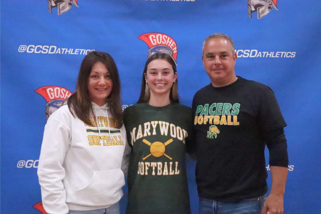 Mia Antolino smiles with her family in front of a Goshen Gladiators background. They are wearing Marywood shirts and sweaters.