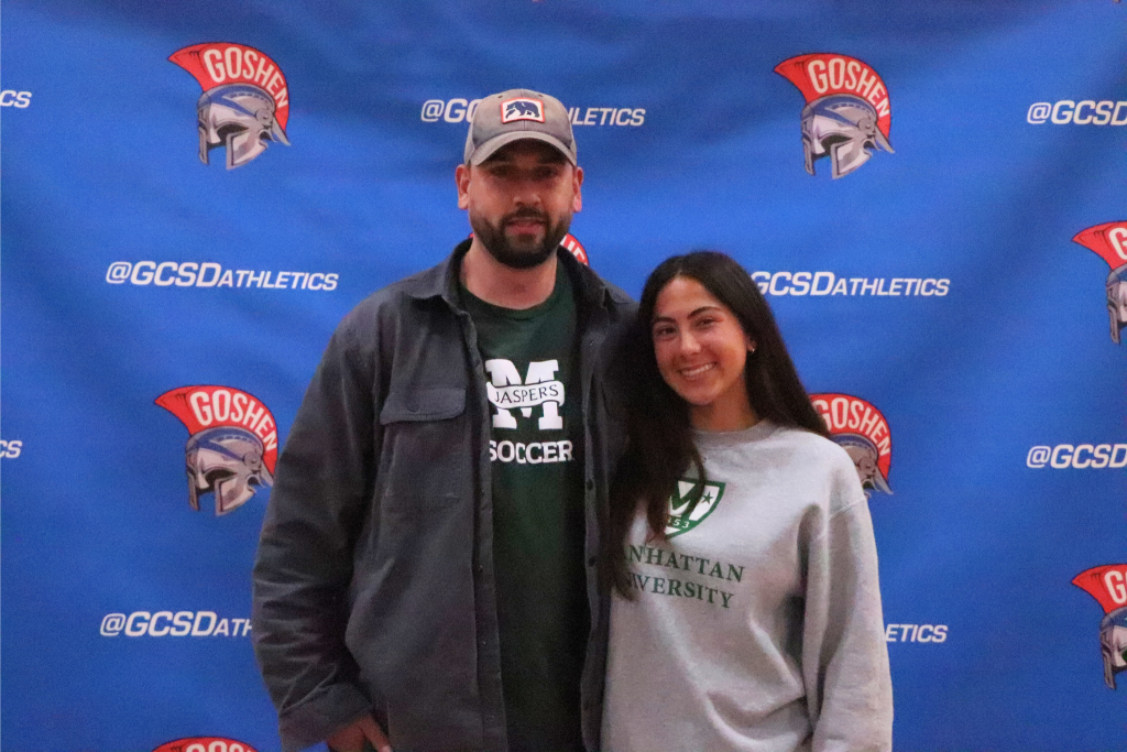 Eryn Primus smiles for the camera with a family member in front of a Goshen Gladiators background.