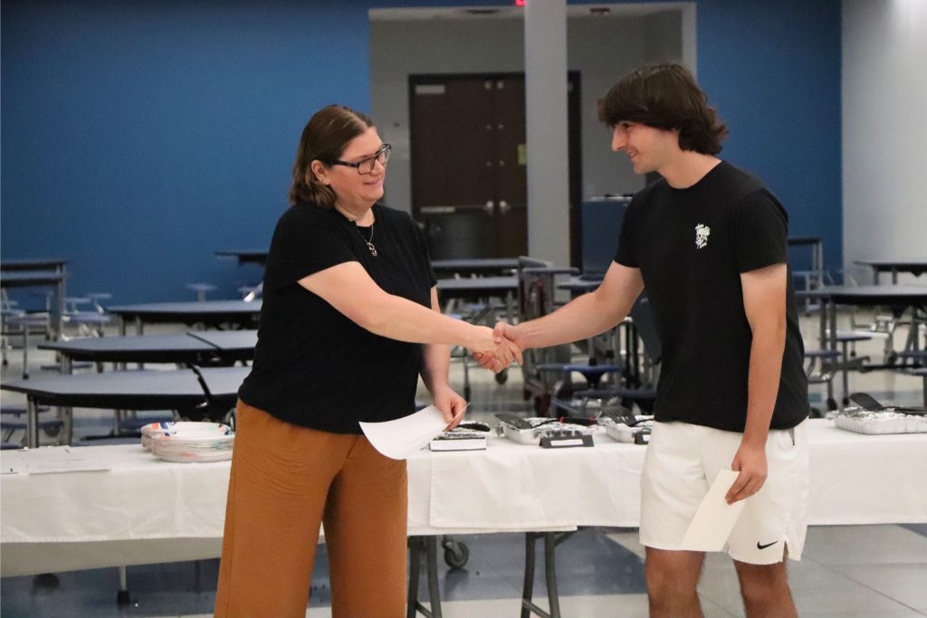 A student shakes hands with a teacher in the cafeteria as she hands them a certificate at the Goshen Greats breakfast.
