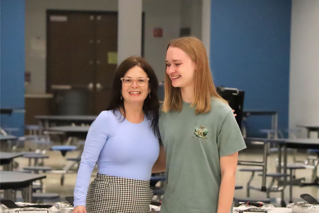 A teacher smiles at the camera with a student who is also smiling in the cafeteria during the Goshen Greats breakfast.