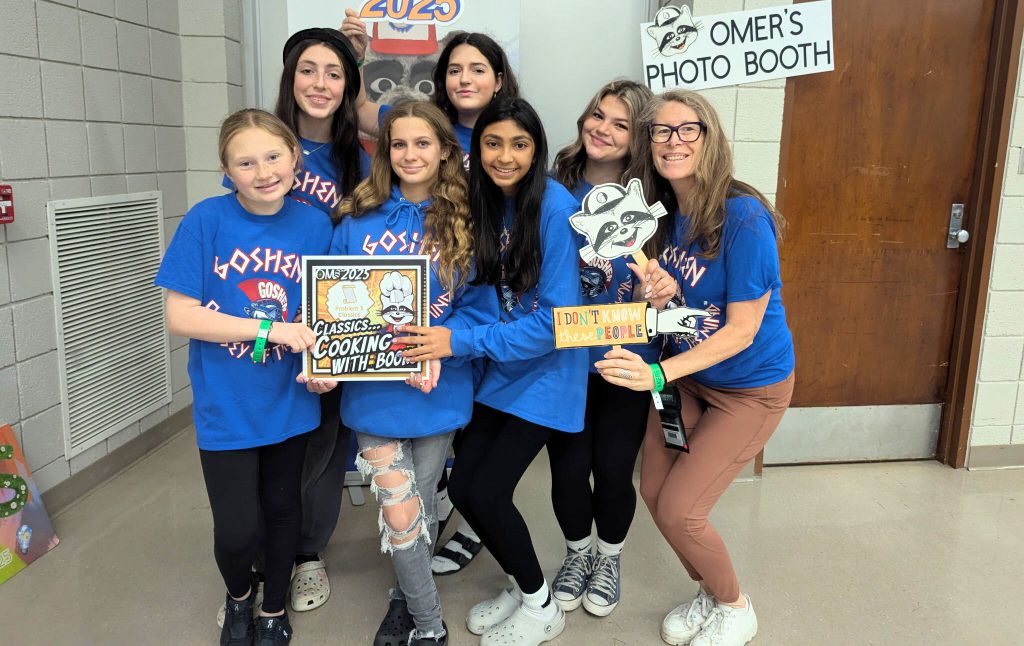 Team Schmidt smiles for a photo in the hallway at World Finals. They are all wearing Goshen Odyssey of the Mind team shirts