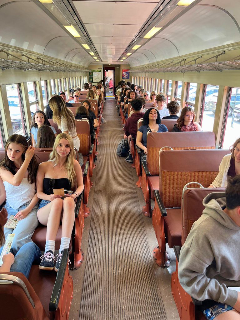Students on a train ride. They are siting in their seats and some are looking at the camera.