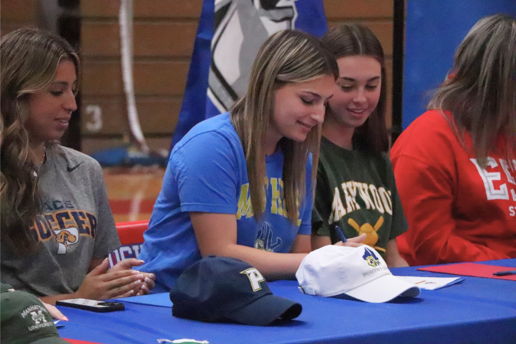 Sophia Appello signs her letter with a Mars Hill hat in front of her and Goshen athletes next to her.
