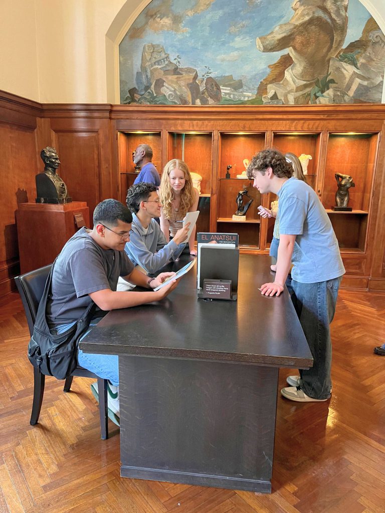 Five students sit around a table and read books and talk.