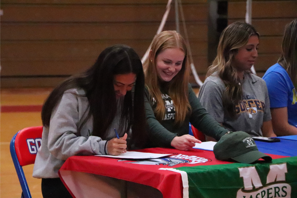 Eryn Primus signs her letter while laughing next to her teammate in Goshen that is also going to Manhattan to play soccer.