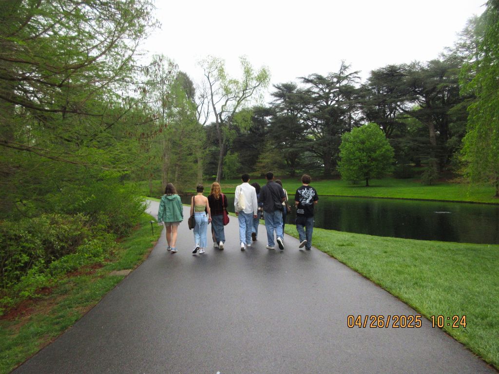 Six students walking down a path with a small lake near them.