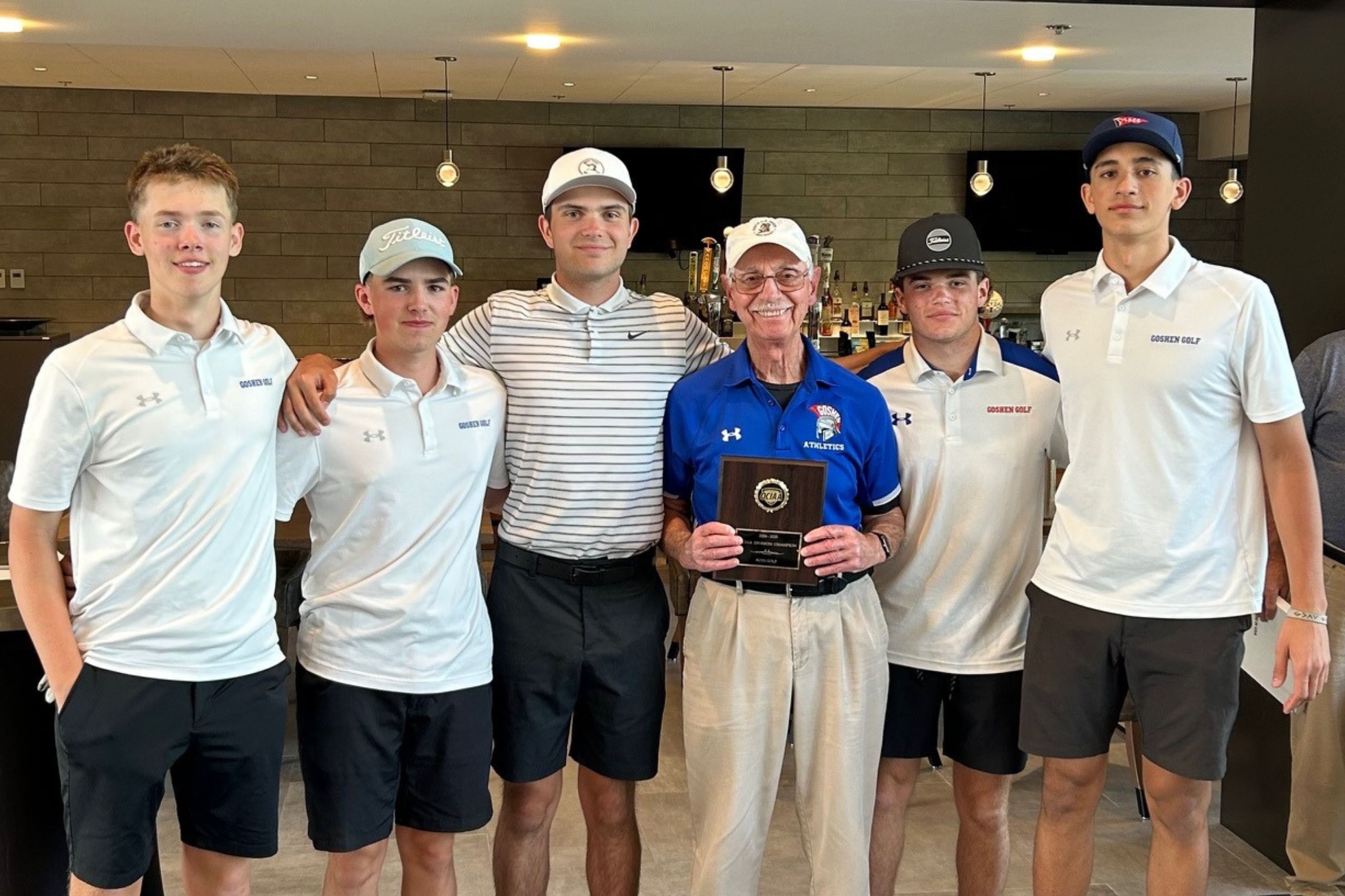 The Goshen Golf team poses with an award. They are all smiling for a photo with white shirts on and looking at the camera.