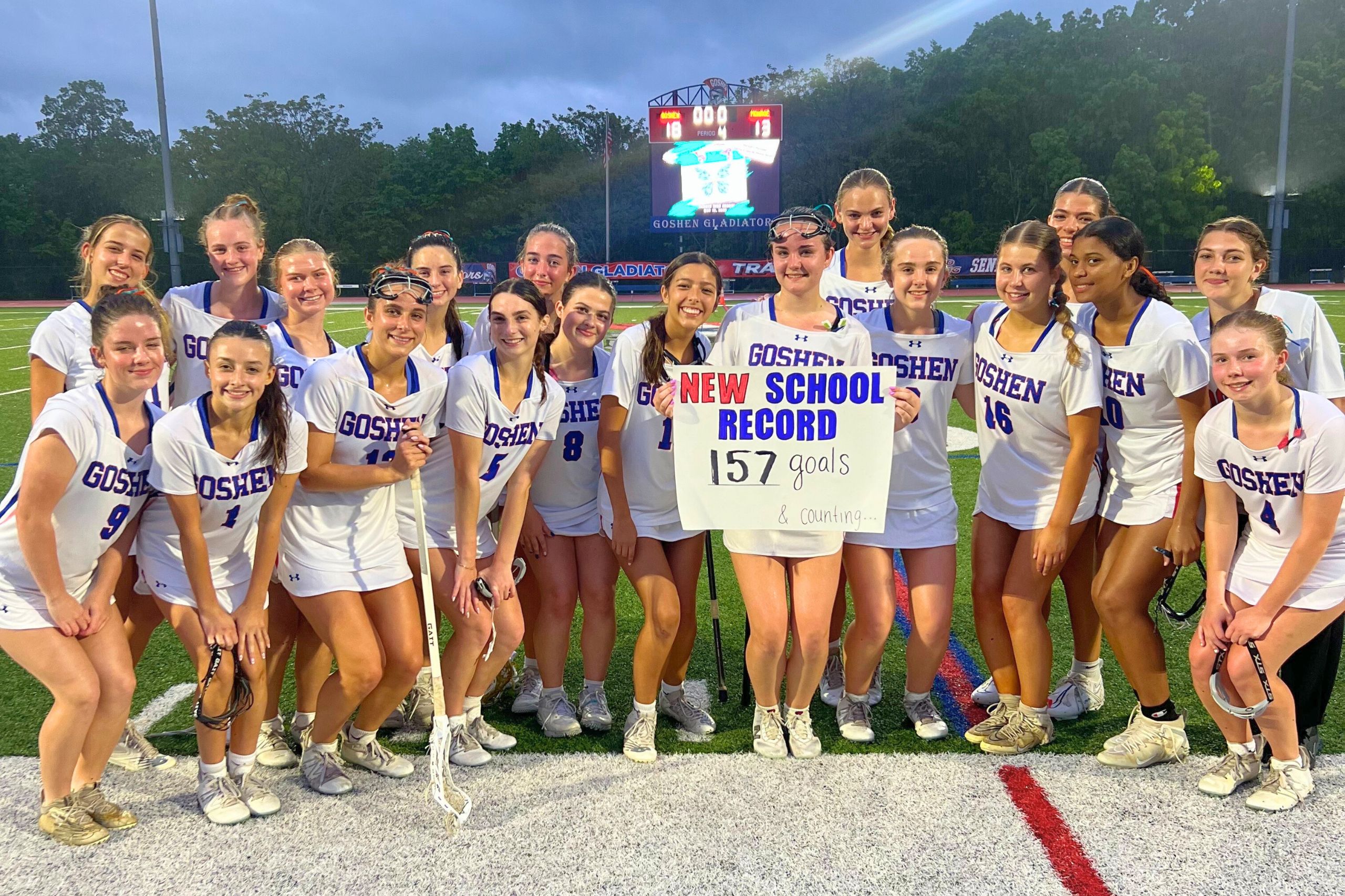 Meghan Doody holds up a sign to celebrate her 157 career goals with her teammates on the field in Goshen