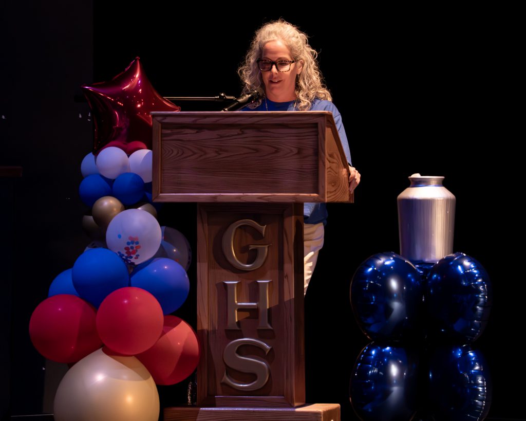 Dr. Heather Hendershot speaks at the podium during the opening ceremony to the Special Olympics. There are balloons to her left and right and the letters GHS are going down the front of the podium.