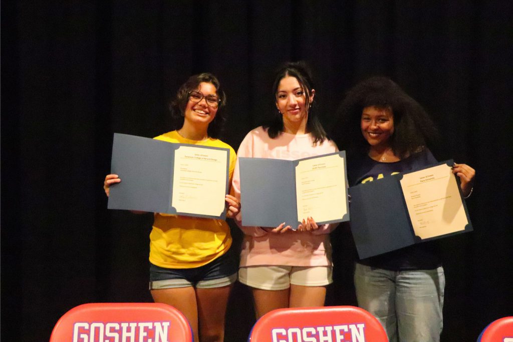Three students hold up their letters that are signed and show their intention to continue their education.
