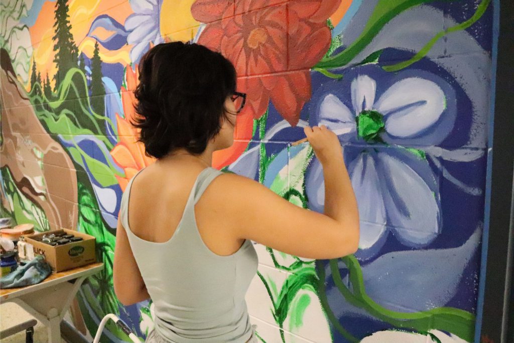 Katie Palau paints a flower on the wall of Goshen High School. The flower is purple and blue.