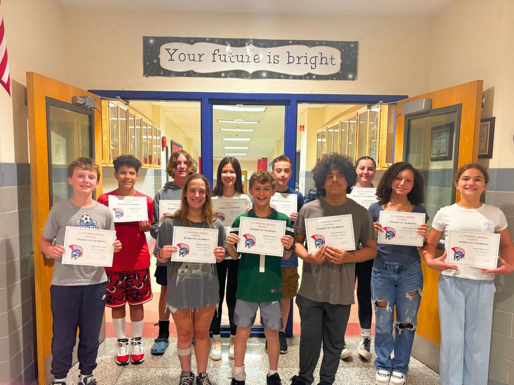 Eleven students stand together in the hallway and show their certificates. They are smiling at the camera.