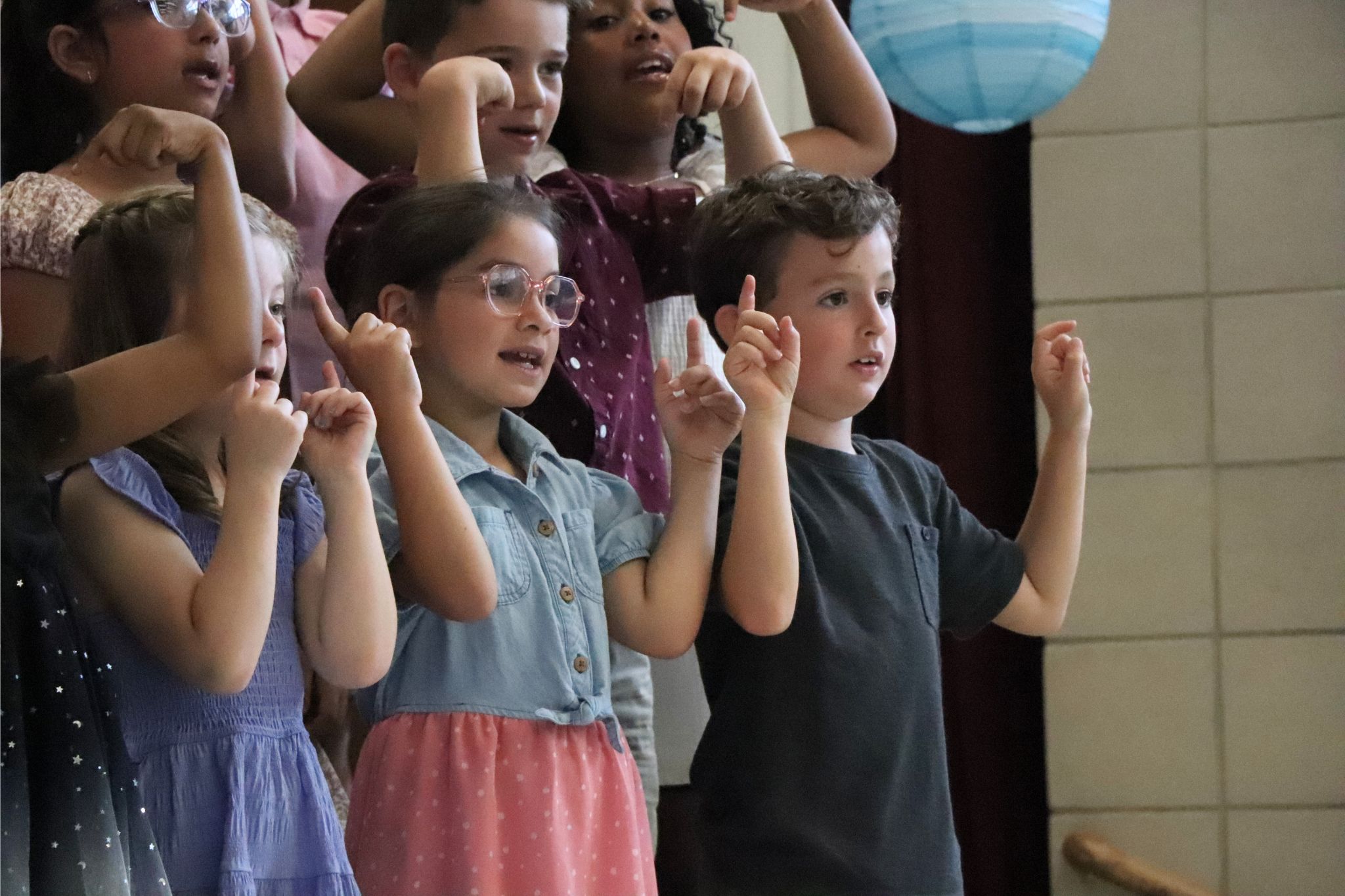 Students are pointing up at the ceiling at the second grade moving up ceremony. 